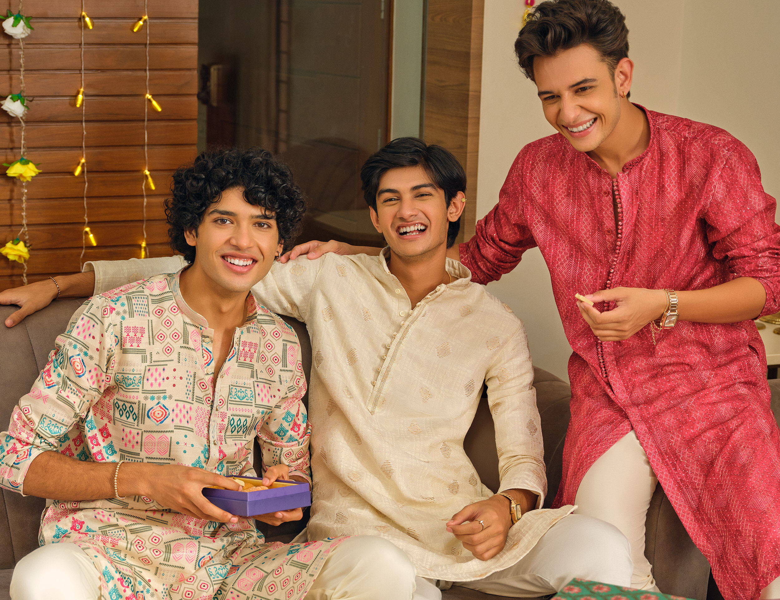 Three men in festive printed and embroidered kurtas celebrate together, showcasing vibrant contemporary ethnic fashion for festive occasions.